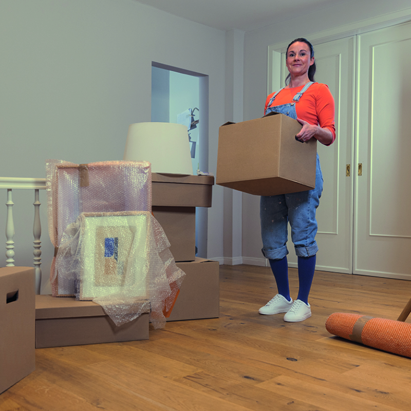A person standing in a living room wearing casual clothes and compression stockings while holding a big box A person standing in a living room wearing casual clothes and compression stockings while holding a big box